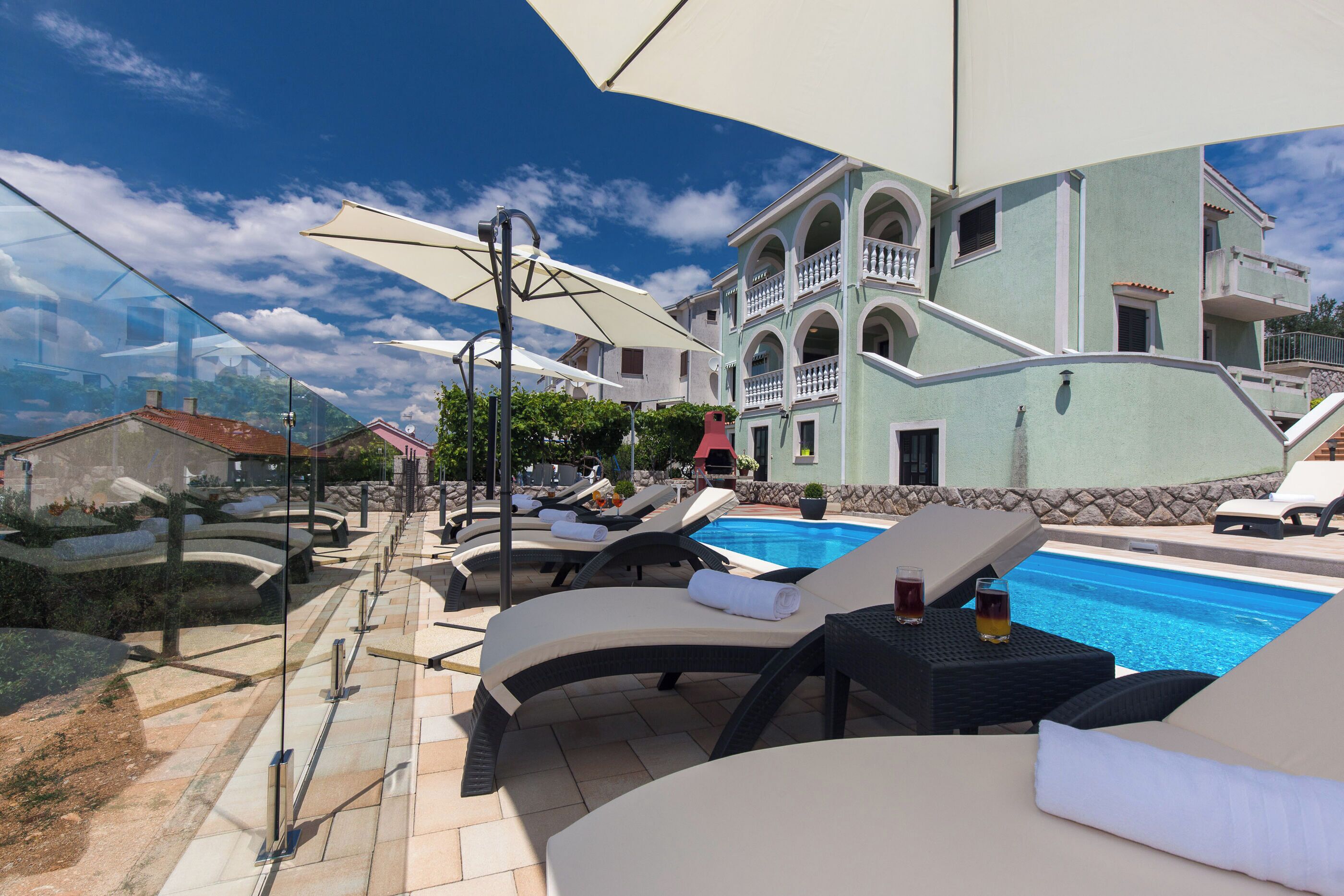 Zona junto a la piscina con sillones, sombrillas y vista despejada de un edificio con balcones.