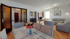 A living room with a sofa, a TV, and a dining table with a vase of flowers. - Apartment Neda (Punat)