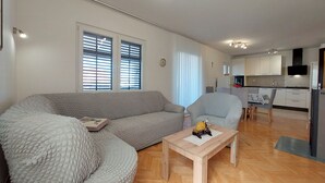A modern living room with a grey sofa, a wooden coffee table, and a dining area with a table and chairs. - Apartment Neda (Punat)