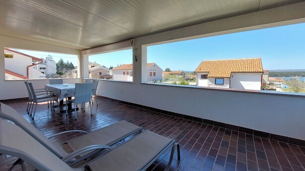 A balcony with a table and chairs, a view of neighboring houses, and a tiled floor. - Apartment Neda (Punat)
