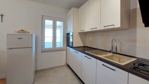 A kitchen with white cabinets, a black countertop, a sink, and a refrigerator. - Apartment Neda (Punat)