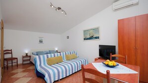 A cozy room with a bed, a TV, a dining table with fruit, and a painting on the wall. - Apartments Jasminka (Selce)