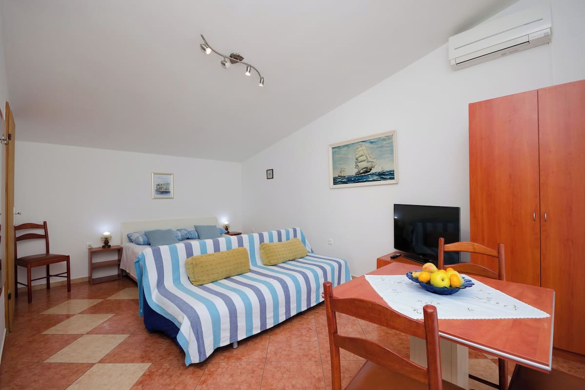 A cozy room with a bed, a TV, a dining table with fruit, and a painting on the wall.