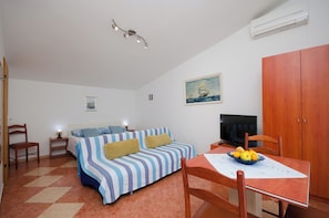 Um quarto aconchegante com uma cama, uma televisão, uma mesa de jantar com frutas e um quadro na parede.