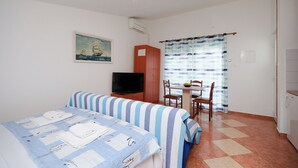 A room with two beds, a TV, a dining table with chairs, and a window with curtains. - Apartments Jasminka (Selce)