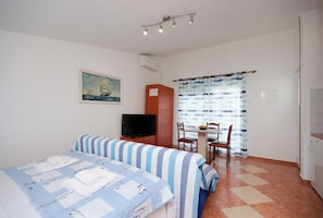 Quarto de hotel com duas camas, televisão, mesa de jantar com cadeiras e janela com cortinas.
