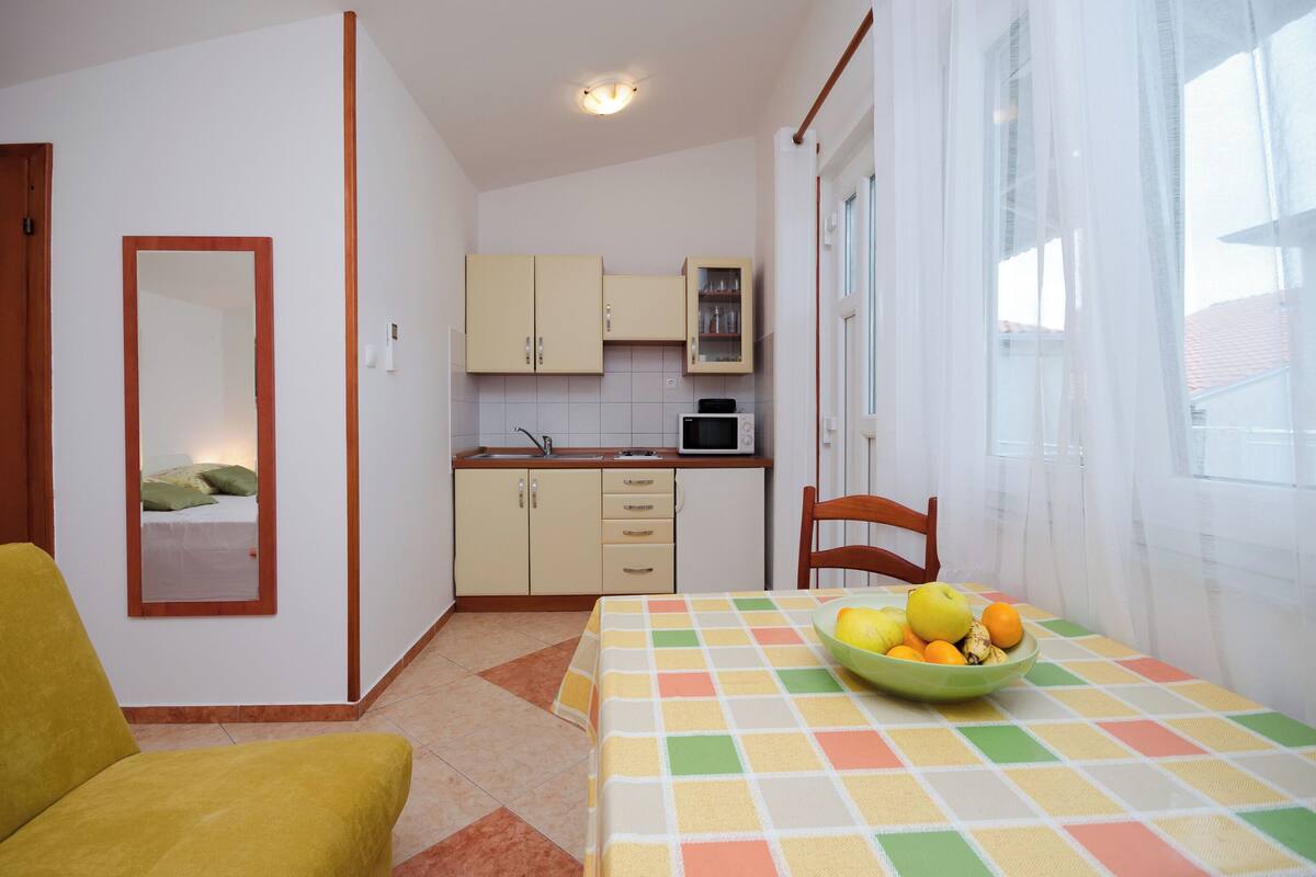 A compact kitchen with cabinets and a microwave, a dining area with a table and chairs, and a window with sheer curtains.