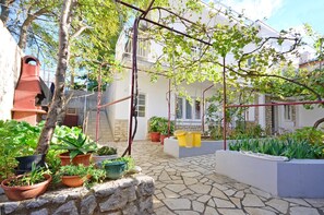 A courtyard with potted plants, a stone floor, and a building with balconies. - Apartments Jasminka (Crikvenica)