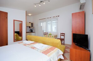 A hotel room with a bed, a TV, a dining table with chairs, and a kitchen area. - Apartments Jasminka (Crikvenica)