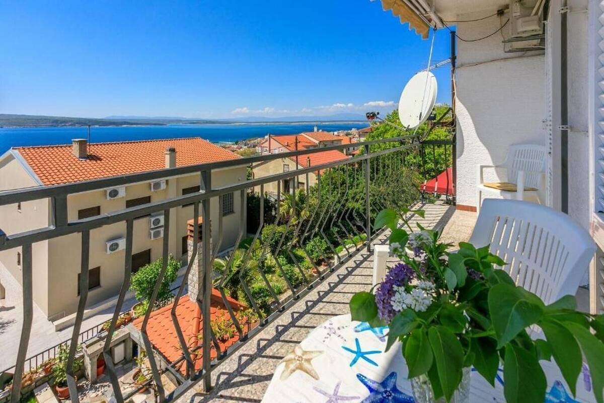 Een balkon met uitzicht op zee, een schotelantenne en bloempotten.