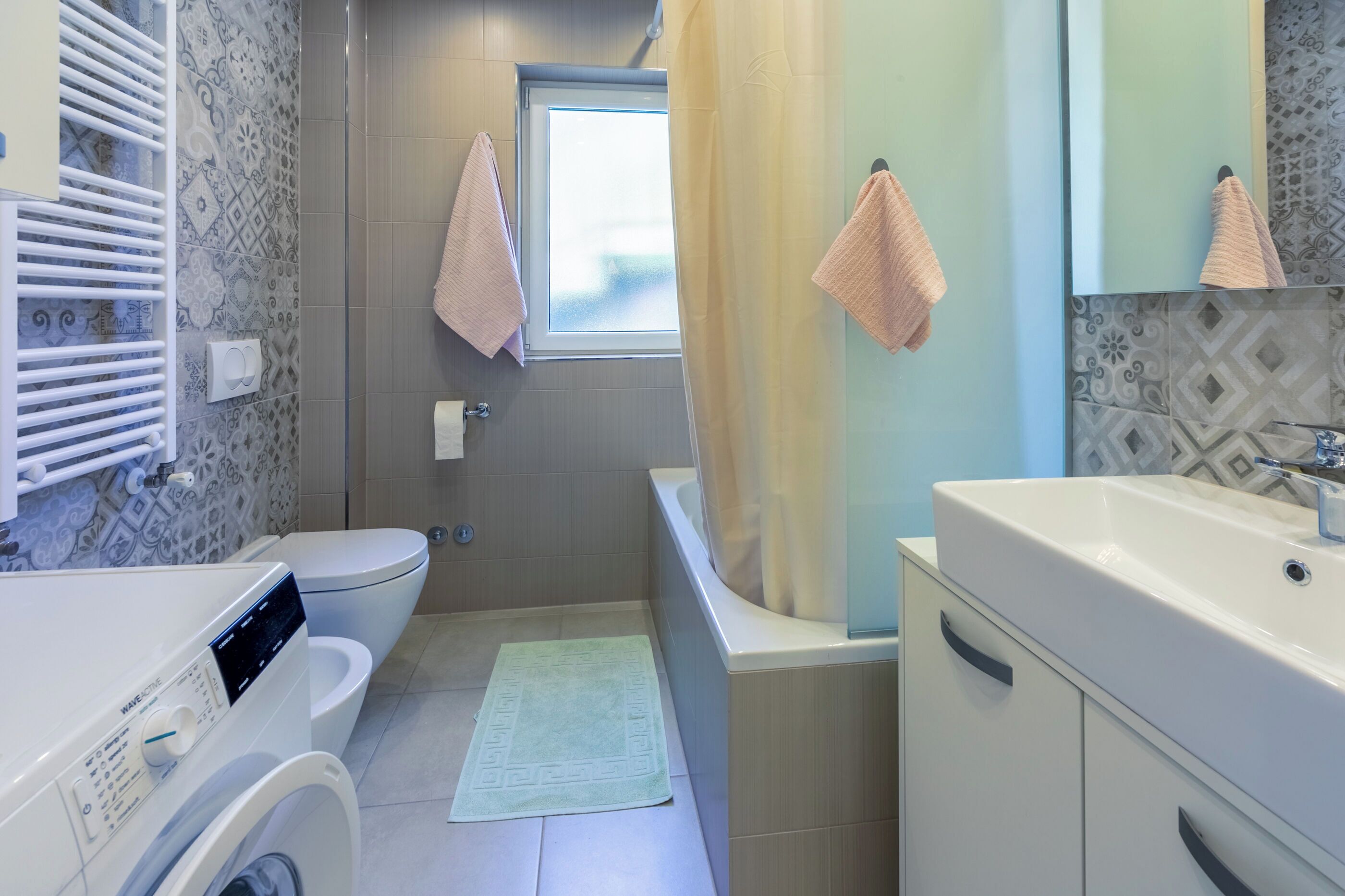Baño pequeño y funcional con inodoro, lavadora, bañera y lavamanos.