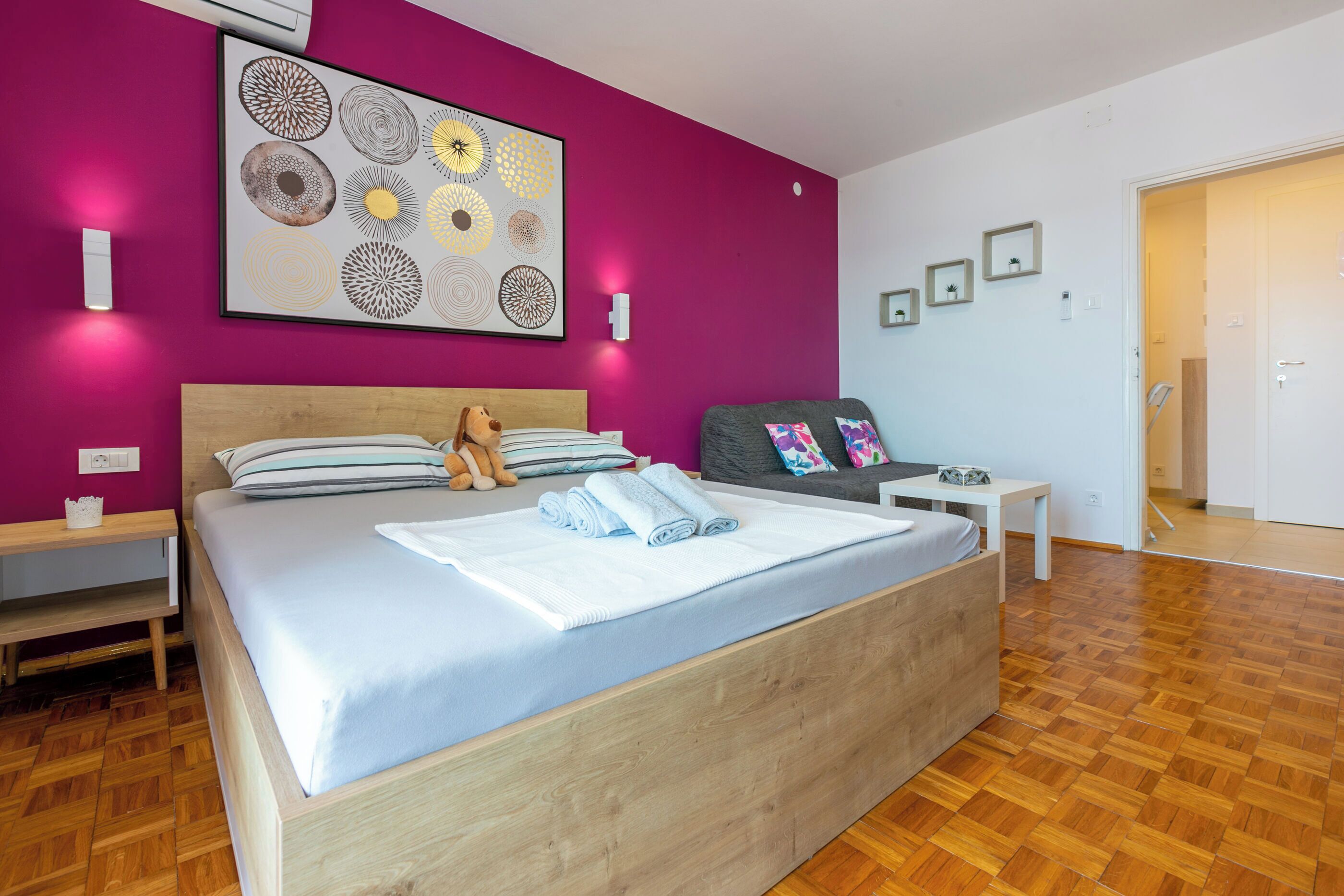 A bedroom with a wooden bed, a large abstract painting, a teddy bear, and a gray sofa.