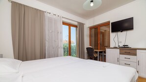 A hotel room with a large bed, a television, a desk with a chair, and a view of the outdoors through a sliding door. - Apartments Dijana (Crikvenica)