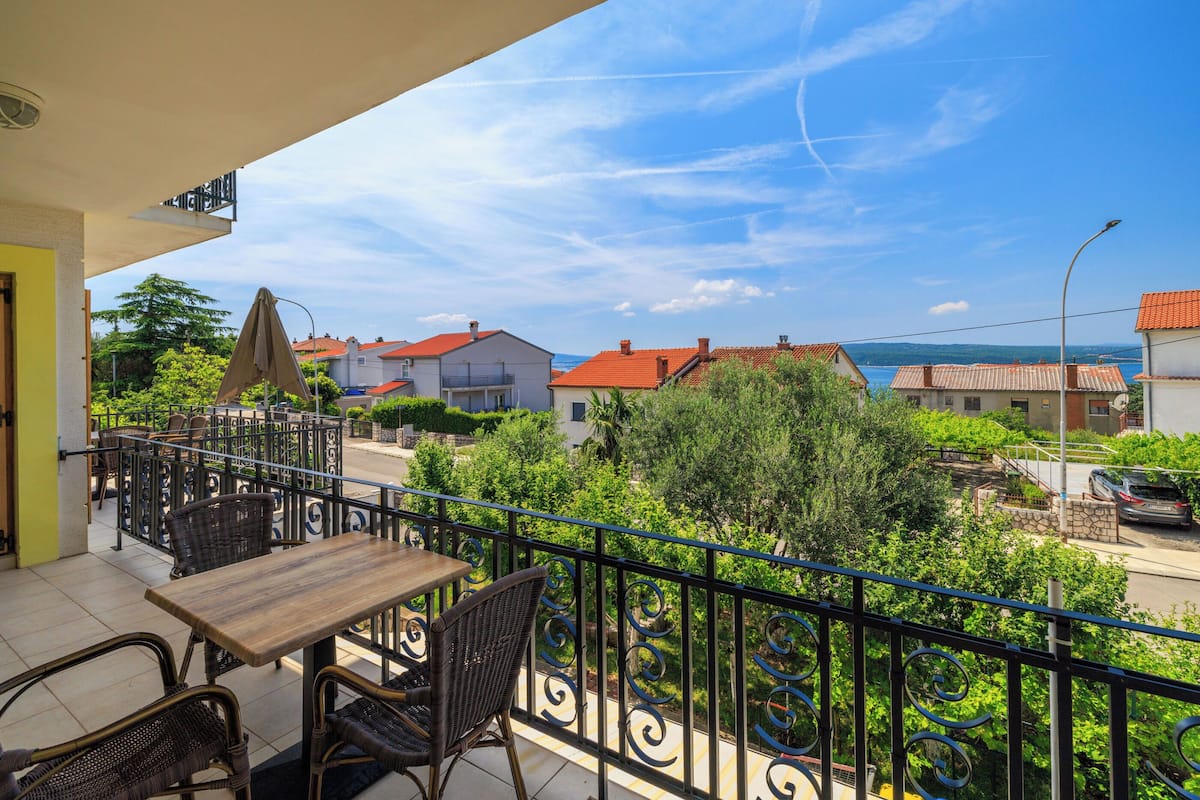 A balcony with a table and chairs, overlooking a residential area with houses and greenery.