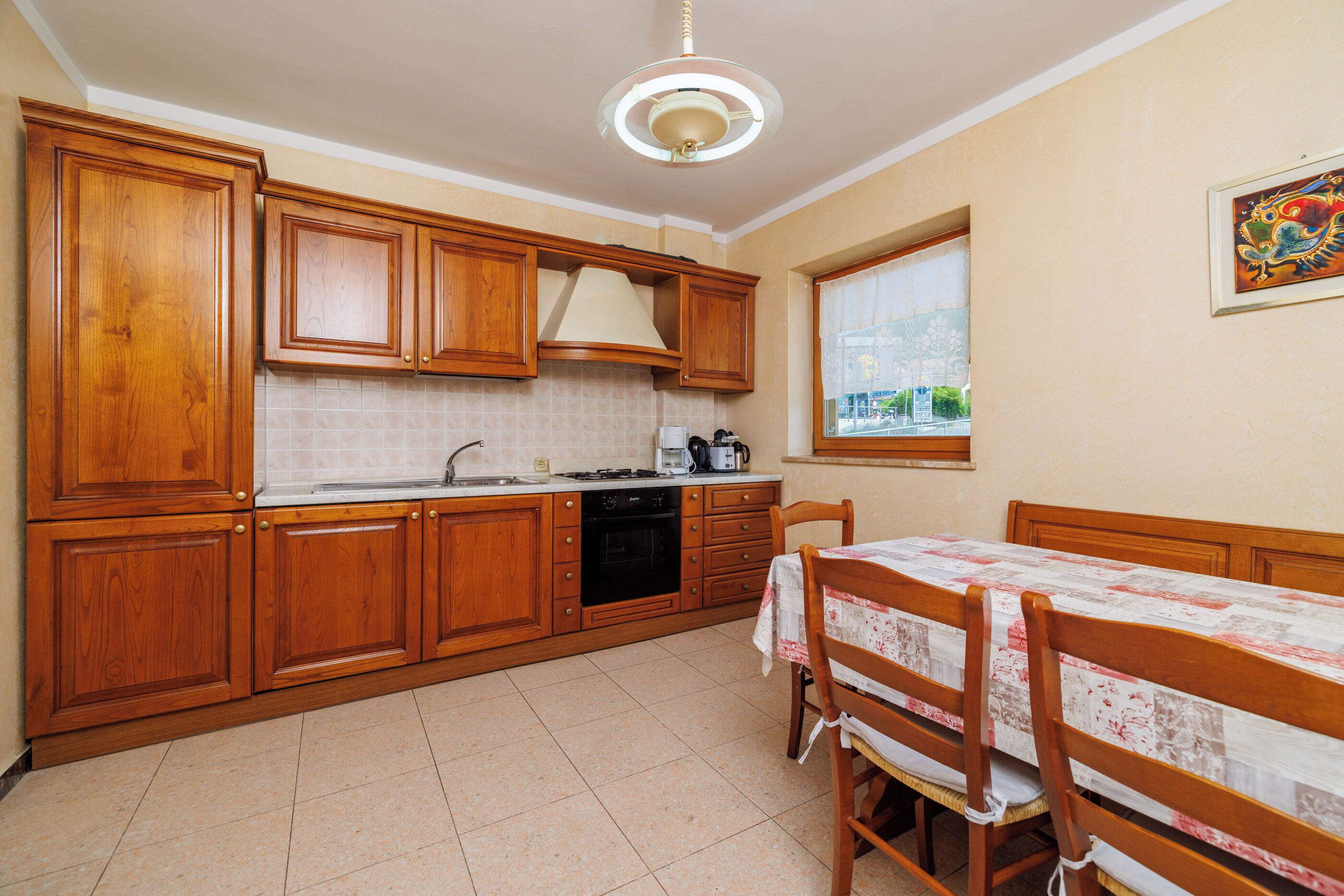 A kitchen with wooden cabinets, a dining table with chairs, a window with a view, and a ceiling light fixture.