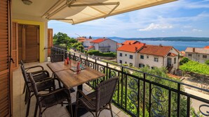 A balcony with a table and chairs, overlooking a coastal town with red-roofed buildings and a view of the sea. - Apartments Dijana (Crikvenica)