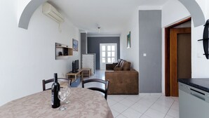 A dining area with a table, chairs, a wine bottle, and glasses. There is a sofa and a television in the background. - Apartment Marica (Lopar)
