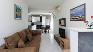 A living room with a brown sofa, a TV on a wooden stand, and a painting of a boat on the wall. - Apartment Marica (Lopar)