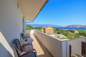 A balcony with a table and chairs, overlooking a coastal landscape with mountains and a clear sky. - Apartment Stojna (Lopar)