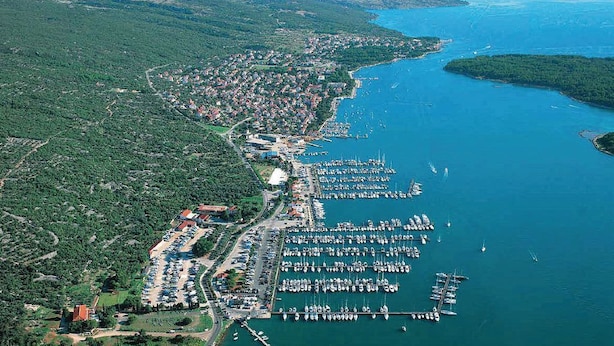 An aerial view of a coastal town with a marina, dense greenery, and a clear blue sea. - Apartments Nikola (Punat)
