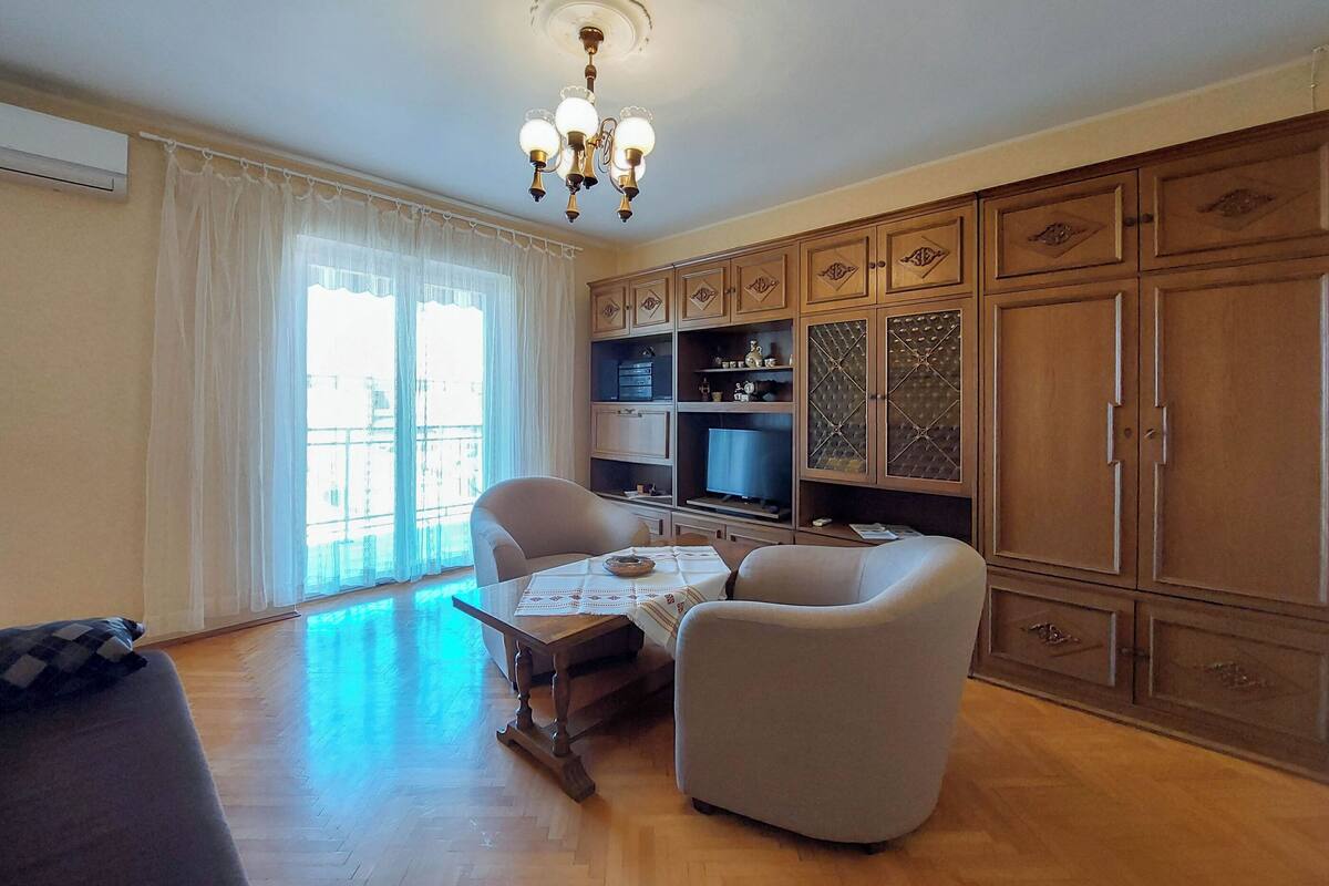 A living room with a wooden floor, a chandelier, a television, and wooden cabinets.