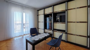 A room with a wooden floor, a black table with a lace tablecloth, two chairs, a sliding shoji screen, and a window with sheer curtains. - Apartments Nikola (Punat)