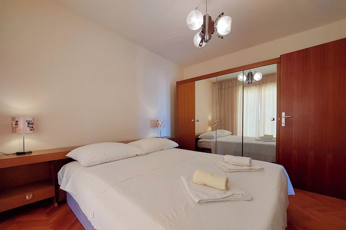 A hotel room with a bed, a nightstand, a mirror, and a wooden wardrobe.