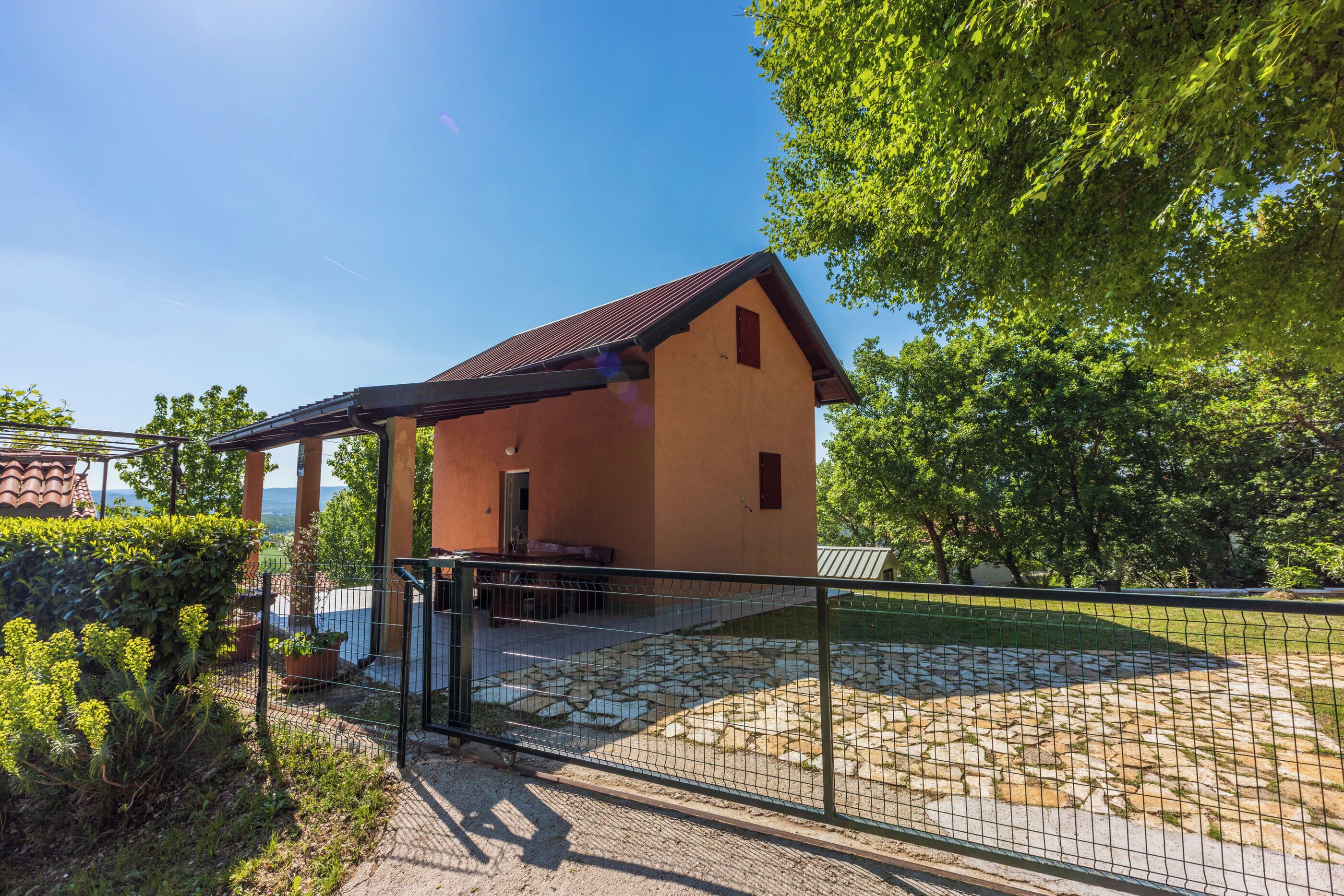 A rustic building with a sloped roof, a covered porch, and a stone-paved area.