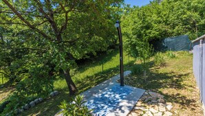 Ένα μονοπάτι στον κήπο με έναν μεταλλικό κίονα φωτισμού, περιτριγυρισμένο από πλούσια βλάστηση και ένα περιμετρικό τοιχίο από πέτρα.