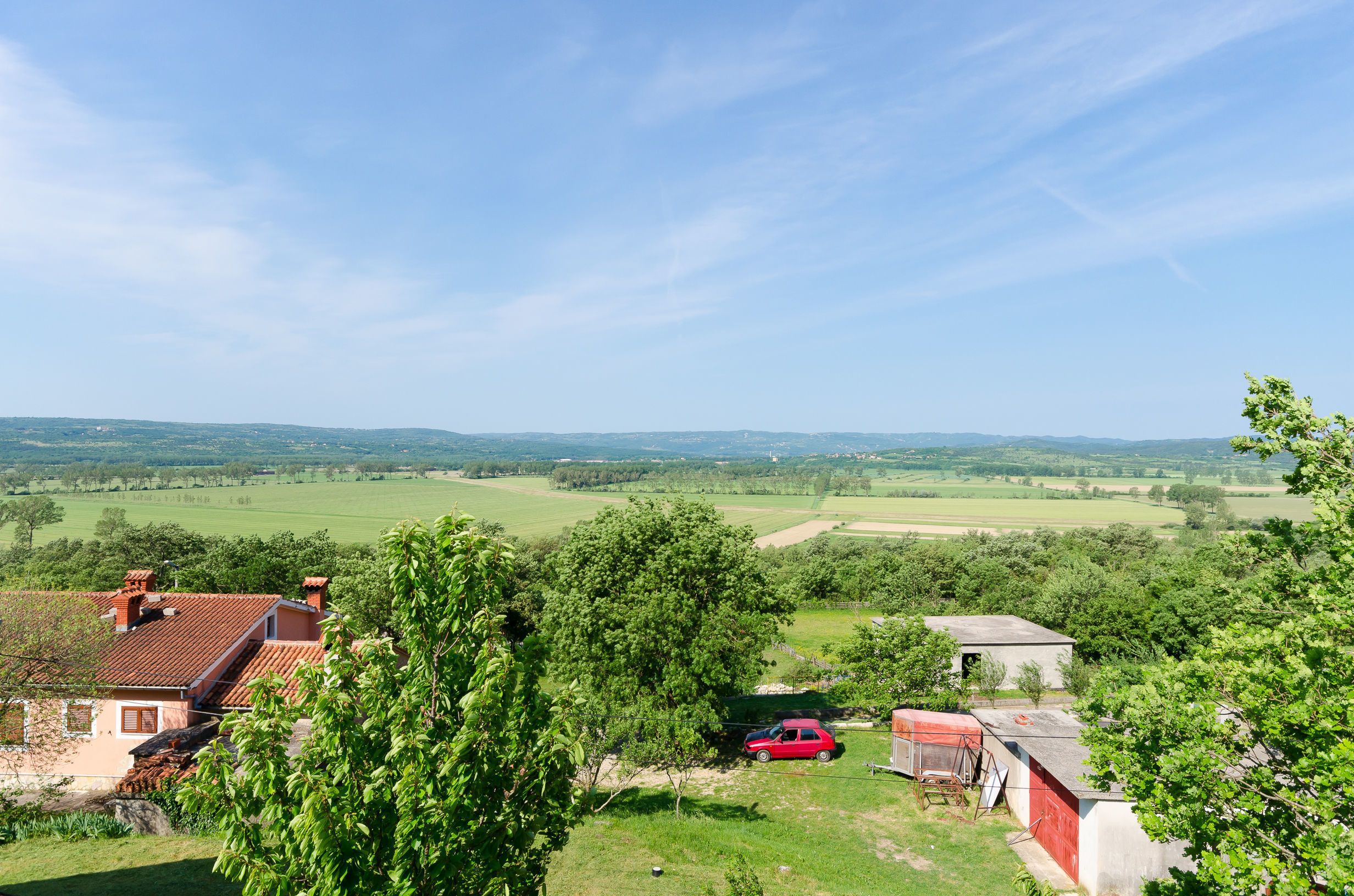 A rural landscape with a red car parked near a house with a red roof.