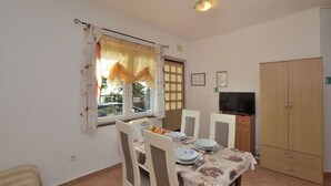 Un coin repas avec une table dressée pour quatre personnes, des chaises, un téléviseur posé sur un meuble et une armoire.