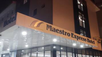 Un hotel llamado "Maestro Express Hotel" con una fachada moderna de vidrio y un letrero rojo que indica que es un hotel.