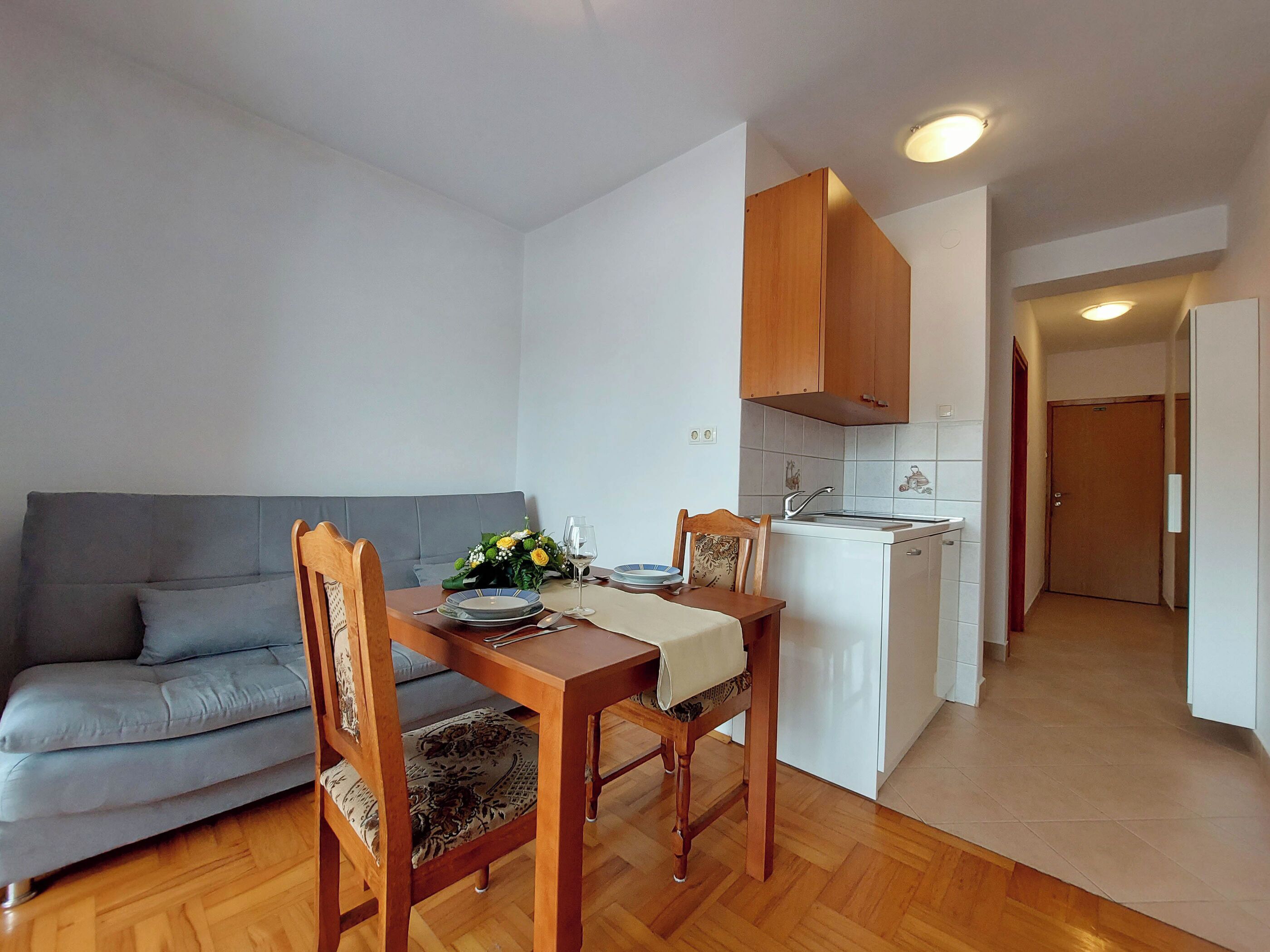 A compact living space with a dining area, kitchenette, and a grey sofa.