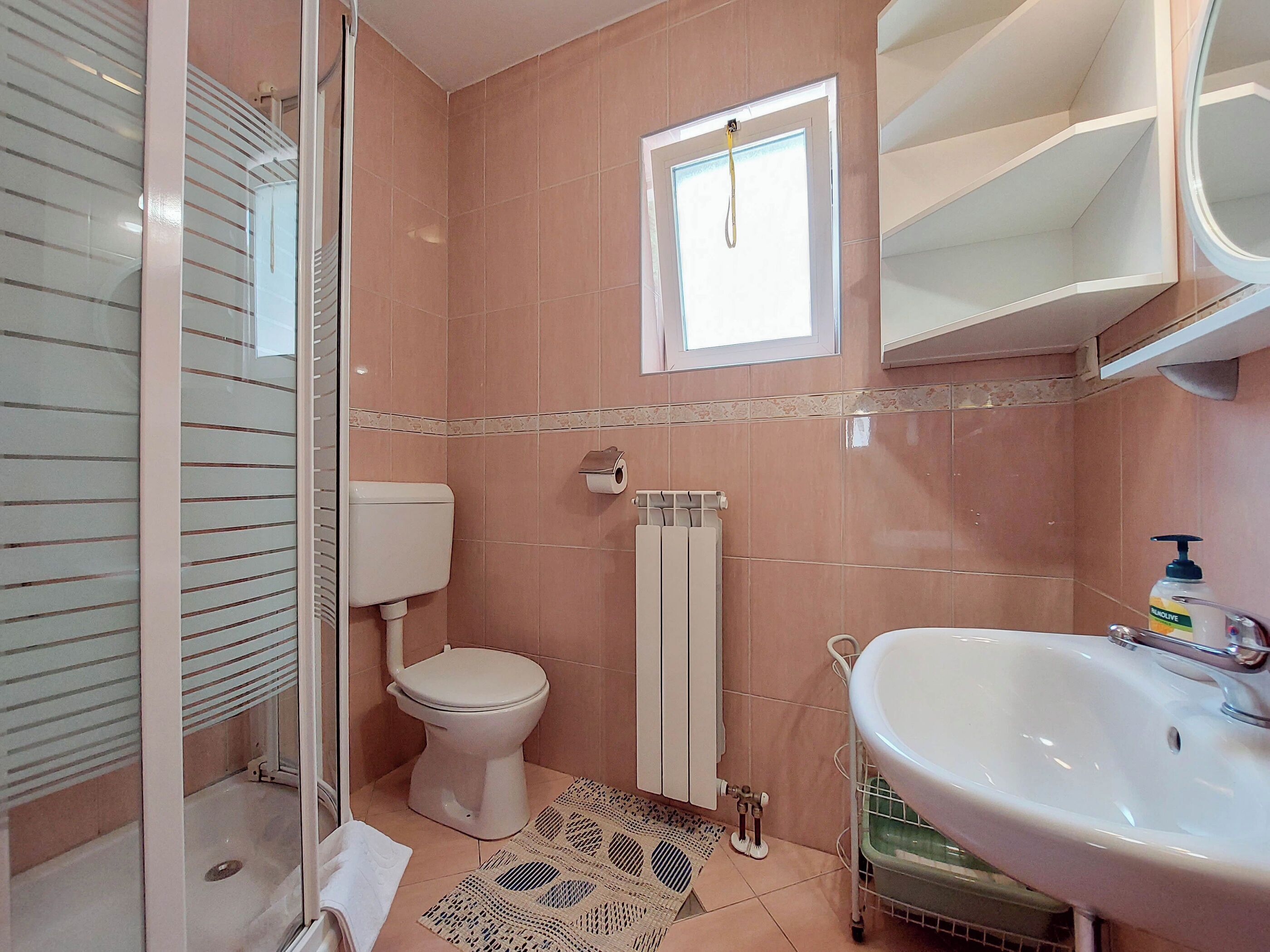 Ein Badezimmer mit Toilette, Heizkörper, Waschbecken und Fenster.