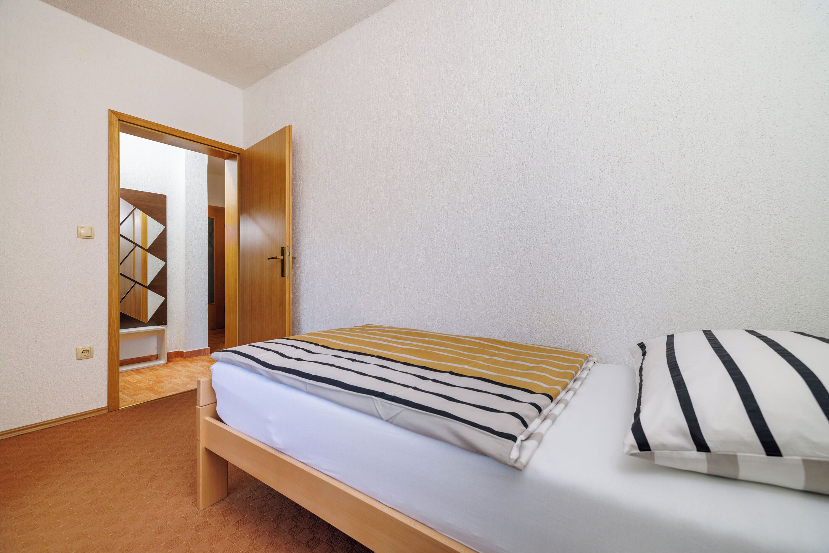 A bedroom with a bed, a wooden headboard, a white wall, and a door leading to a staircase.