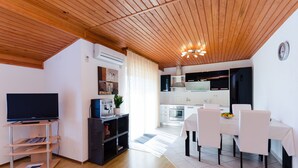 Uma sala de estar moderna com televisão de tela plana, móvel para home theater em madeira e uma área de jantar com mesa e cadeiras brancas.