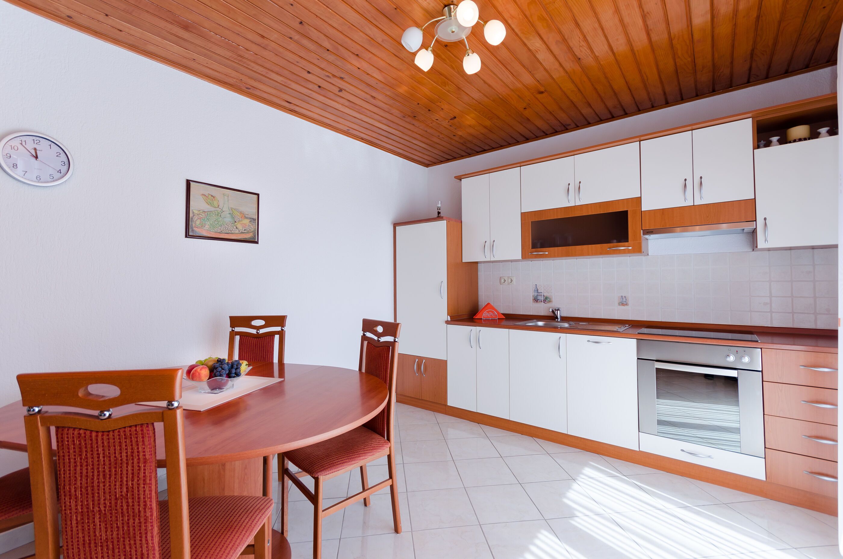 Una cocina moderna con armarios de madera, horno empotrado y comedor con mesa y sillas de madera.