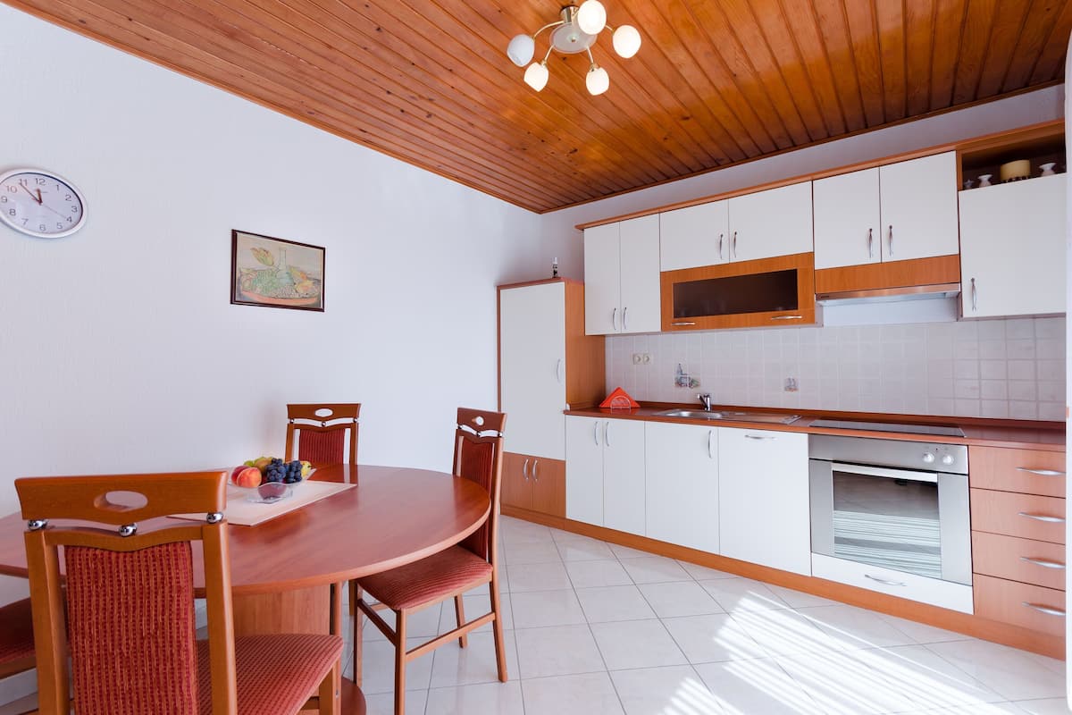A modern kitchen with wooden cabinets, a built-in oven, and a dining area with a wooden table and chairs.
