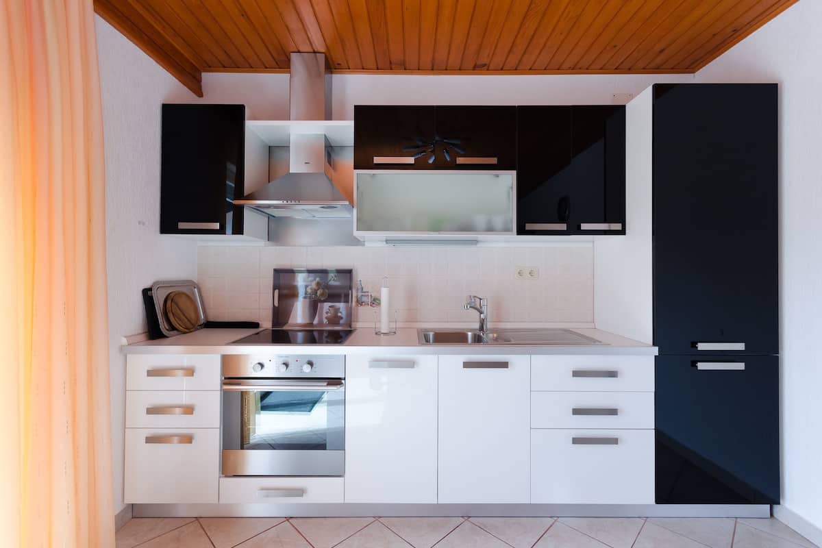 A modern kitchen with white cabinetry, a stainless steel oven, a built-in microwave, and a black refrigerator.