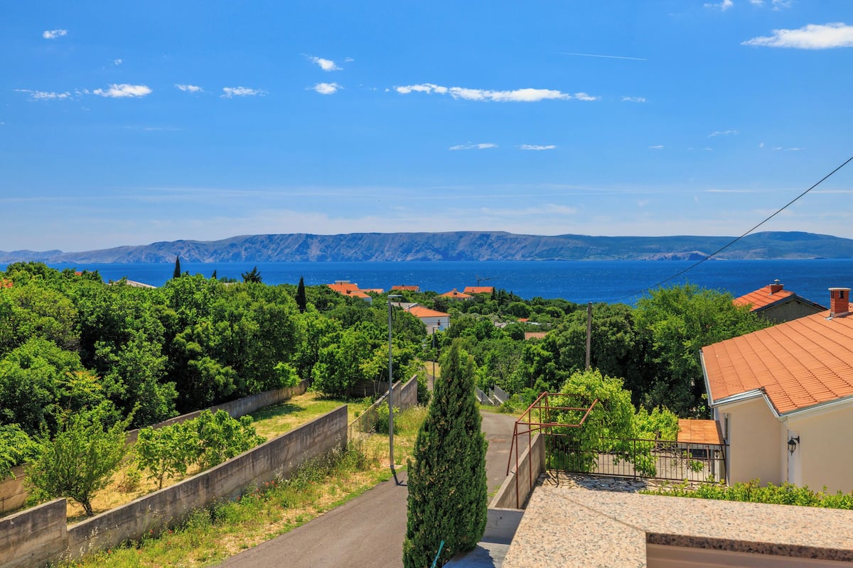 A residential area with houses, a road, and a view of the sea and mountains.