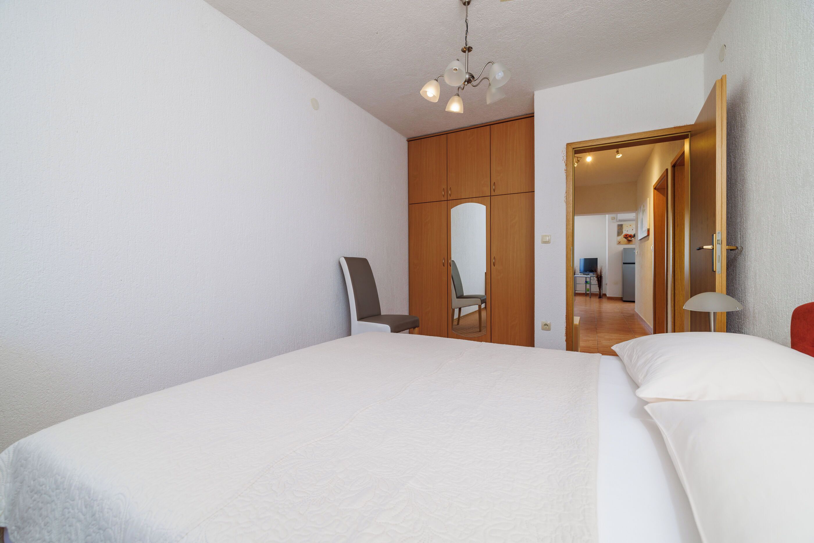 A bedroom with a bed, a chair, a wardrobe, and a mirror.
