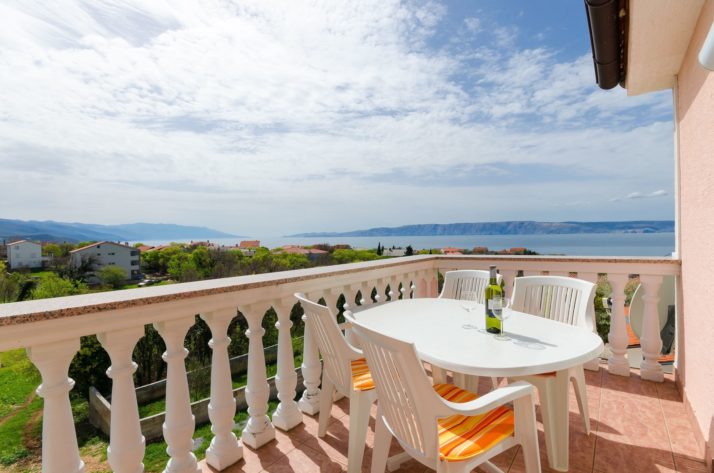 A balcony with a white table and chairs, overlooking a scenic view of a body of water and distant mountains.