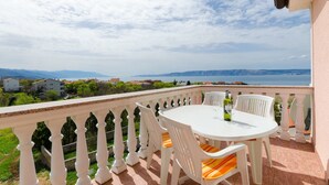 Varanda com mesa e cadeiras brancas, oferecendo uma vista panorâmica de um corpo d'água e montanhas ao longe.