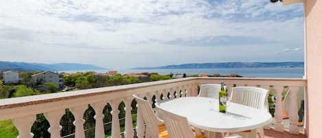 Ein Balkon mit weißem Tisch und Stühlen, der einen schönen Blick auf ein Gewässer und ferne Berge bietet.