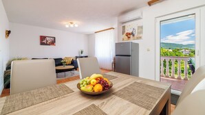 Uma área de refeições com uma mesa posta para dois, uma cesta de frutas e vista para uma varanda com corrimão.