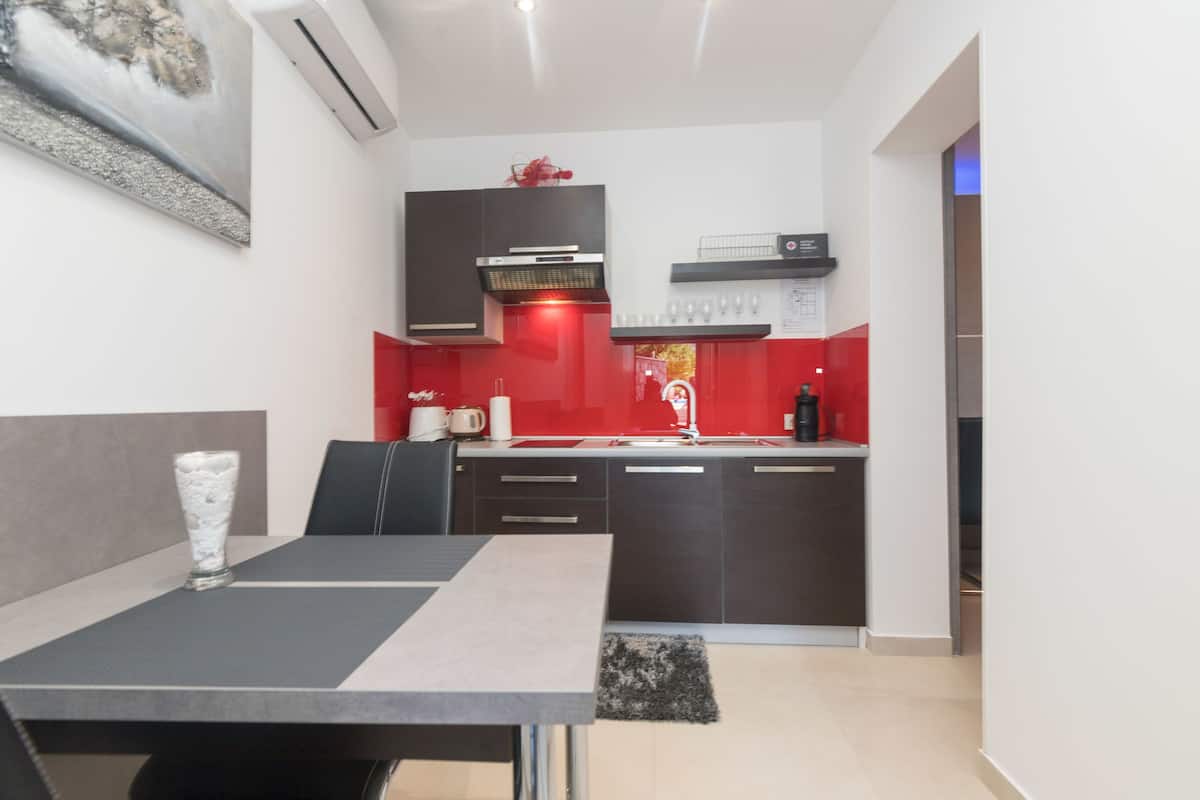 A modern kitchen with dark cabinets, a red backsplash, and a dining area with a table and chairs.