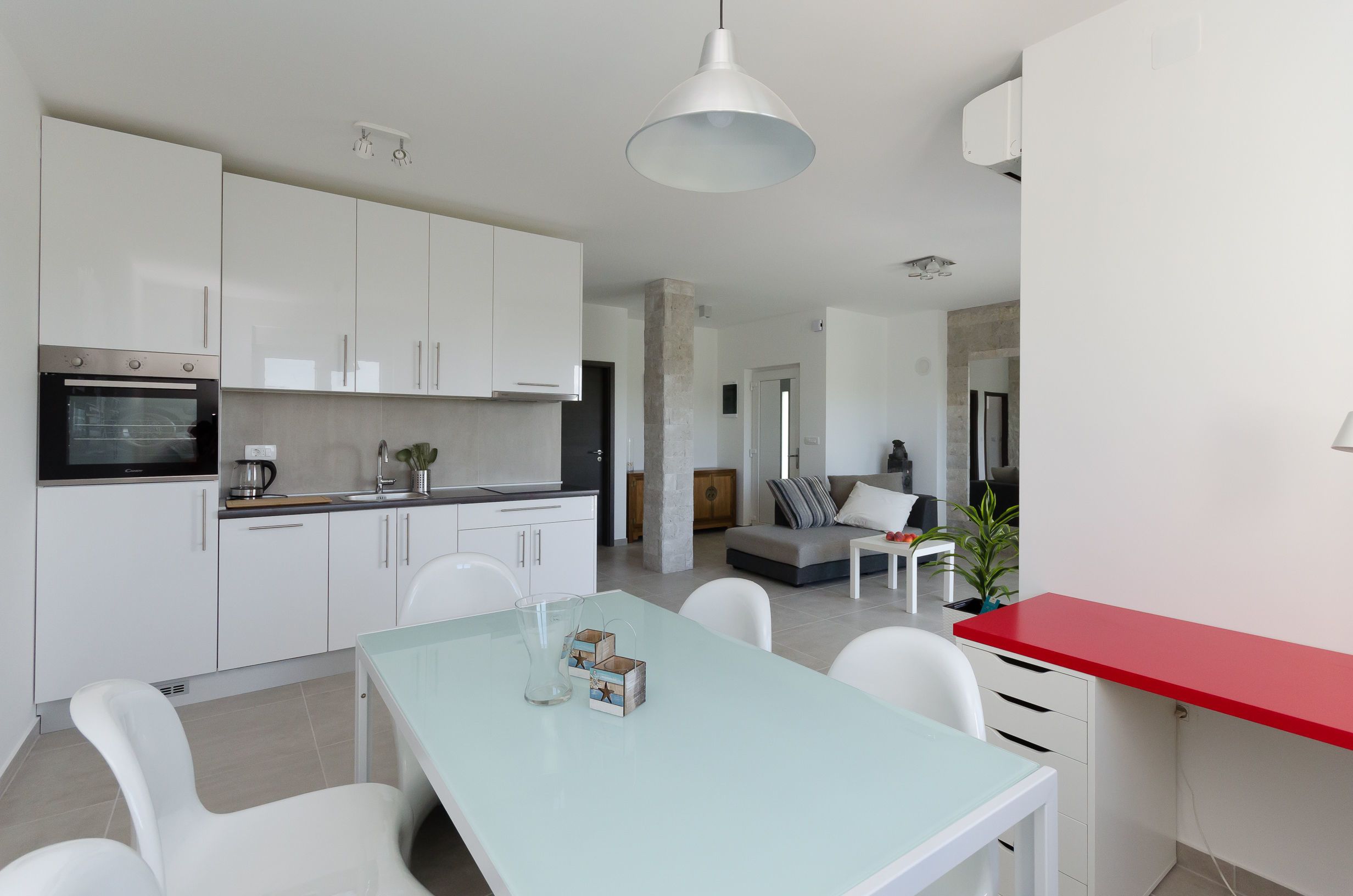 Una cocina moderna con armarios blancos, horno empotrado y comedor con una mesa azul claro y sillas blancas.