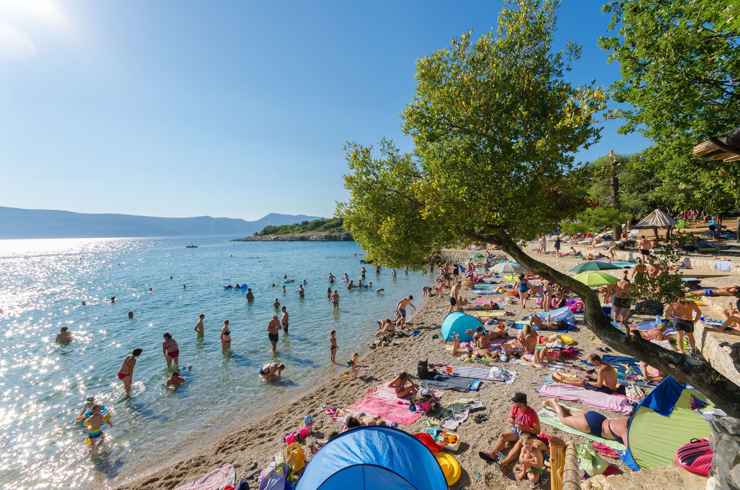 A beach with clear water, people swimming, and tents set up for shade.