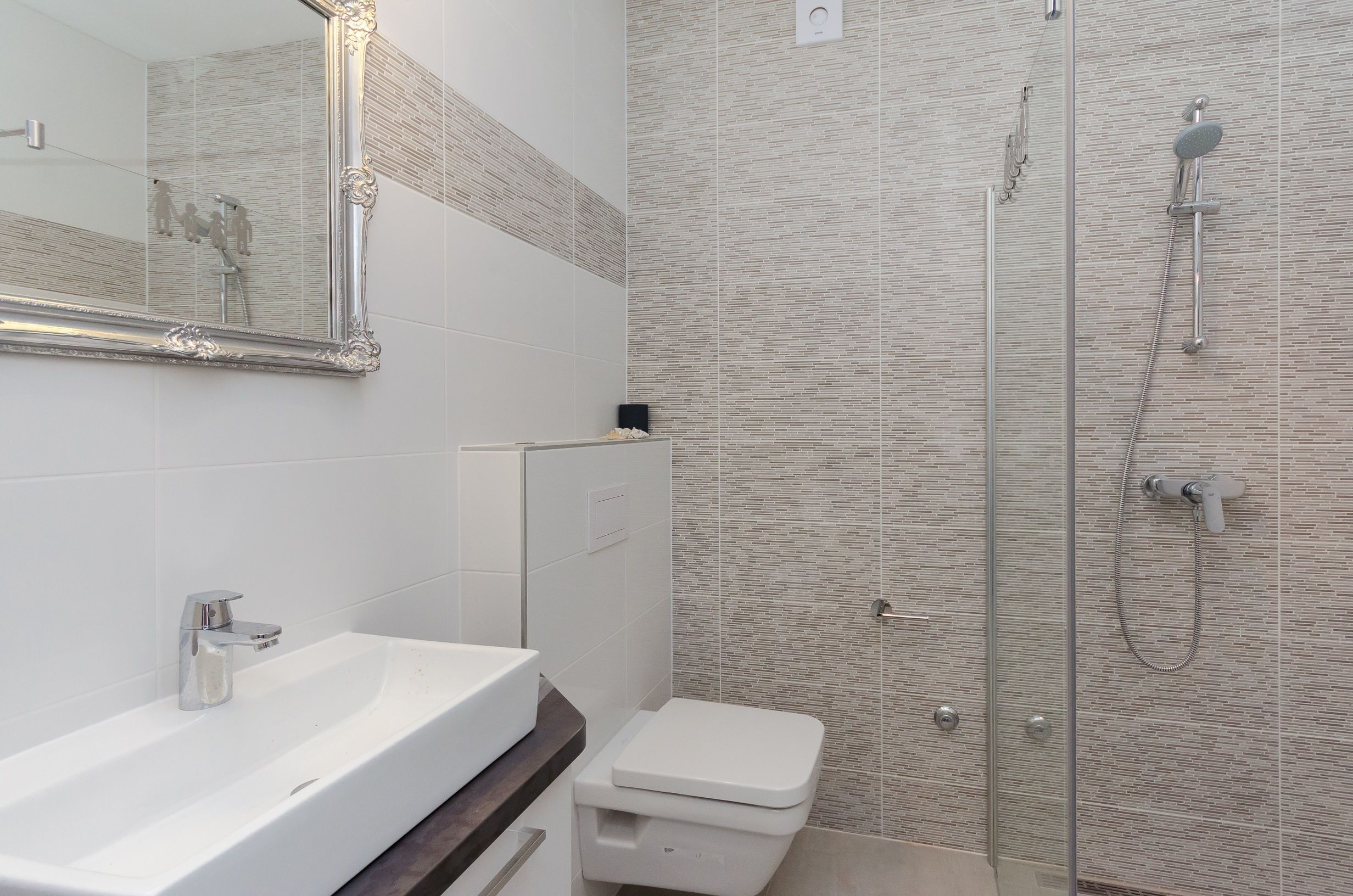 Une salle de bain moderne avec un lavabo blanc, des toilettes et une douche séparée par une paroi de verre.