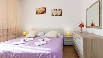 A neatly arranged bedroom with a bed, bedside tables, a dresser, and two wall-mounted paintings.